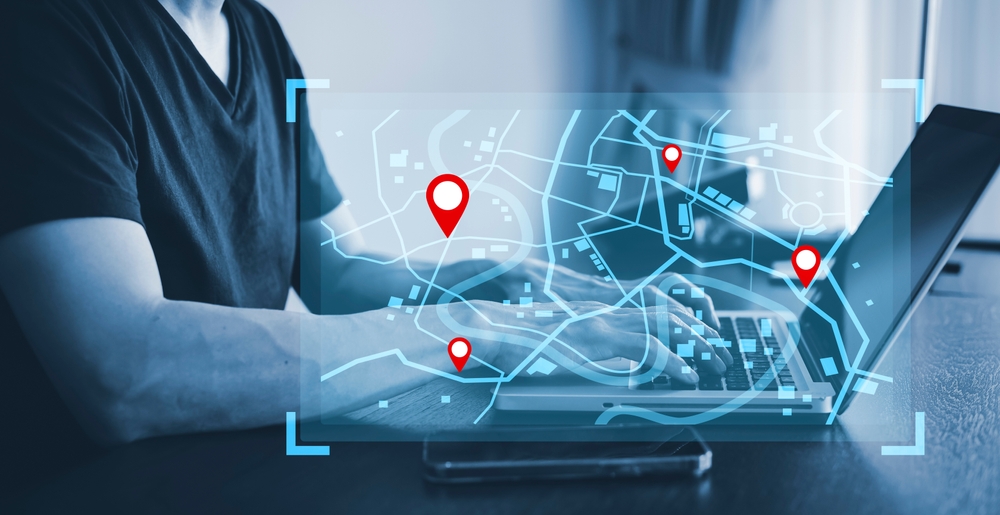 A person using a laptop with a digital map overlay on the screen, displaying red location pins. The scene conveys technology and navigation themes.