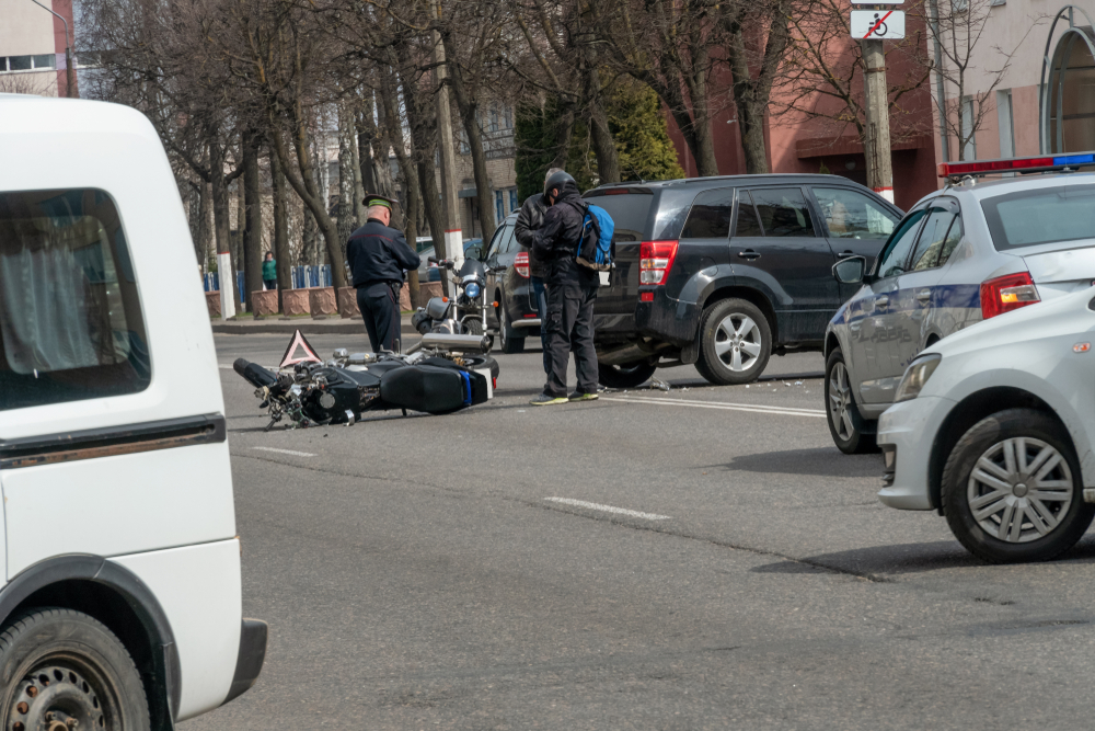 Motorcycle accident scene on a city street, involving a black SUV and a fallen bike. Police officers and a rider assess the situation, conveying tension.