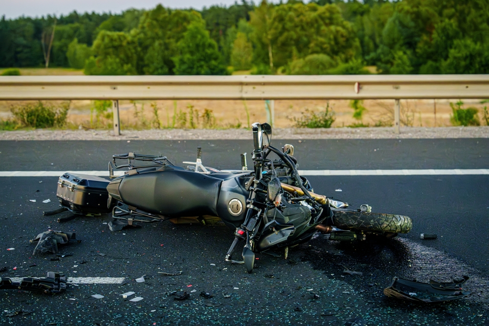 A black motorcycle lies damaged on its side on a road, with debris scattered around.
