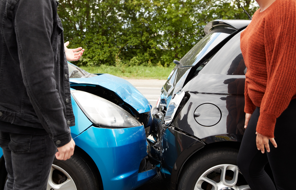 A blue hatchback and a black car involved in a rear-end accident on a roadside.
