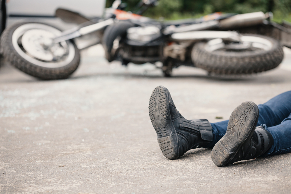 Motorcyclist lying on the road after a motorcycle accident, with the damaged motorcycle visible in the background.