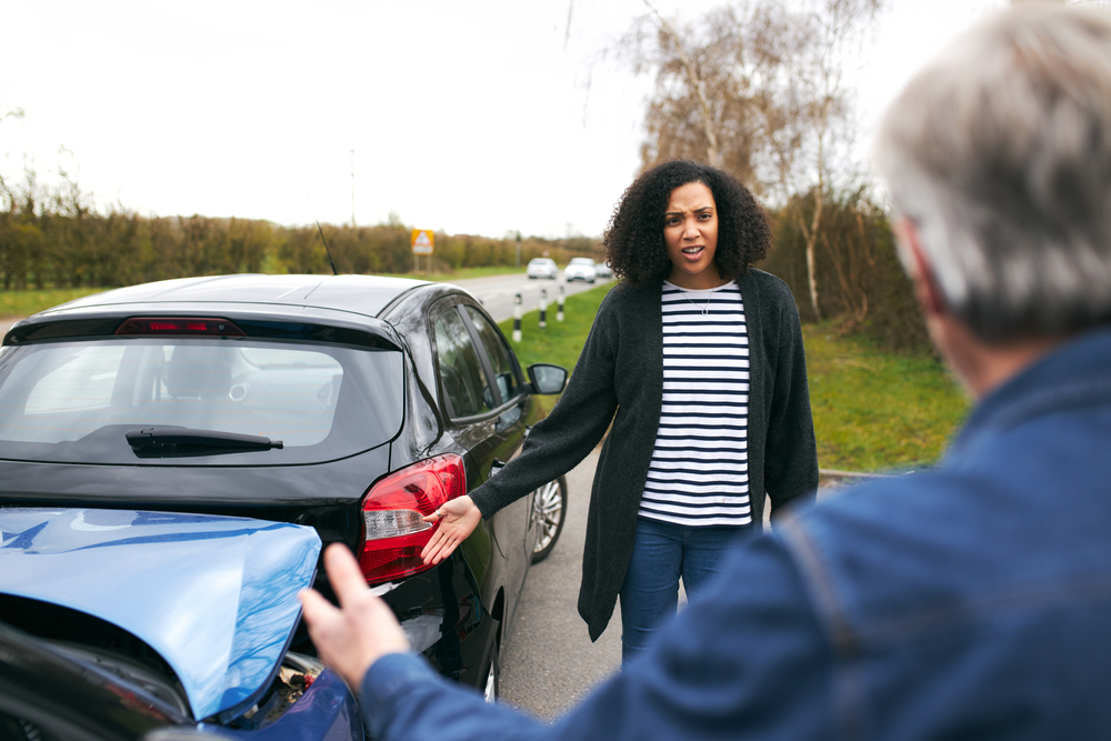 An angry female driver arguing with an older male driver after a rear-end car accident.