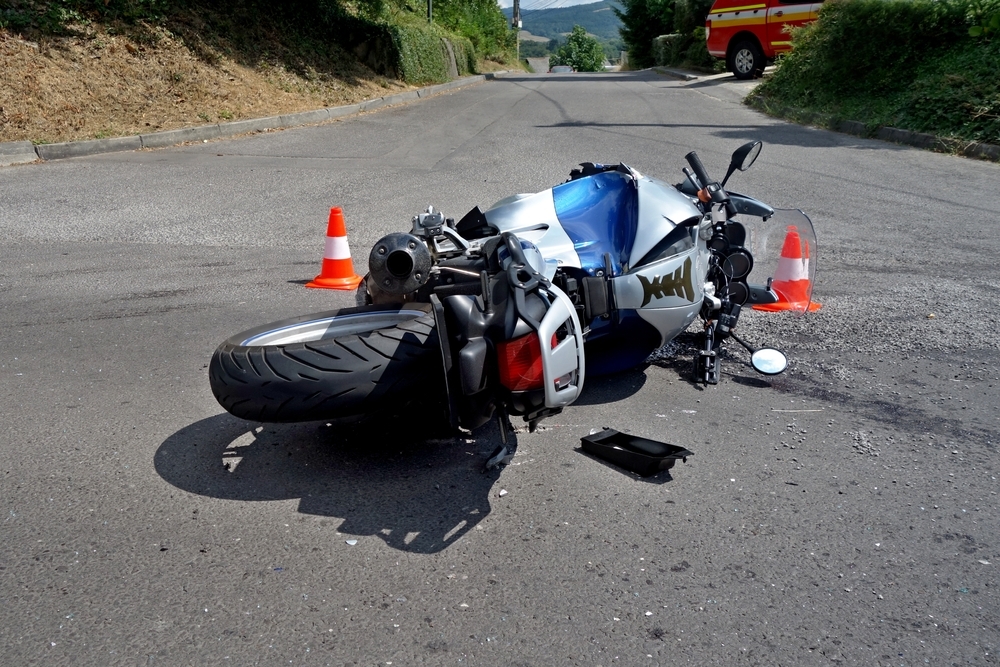 Damaged motorcycle lying in the road after a traffic accident, with traffic cones marking the crash scene.