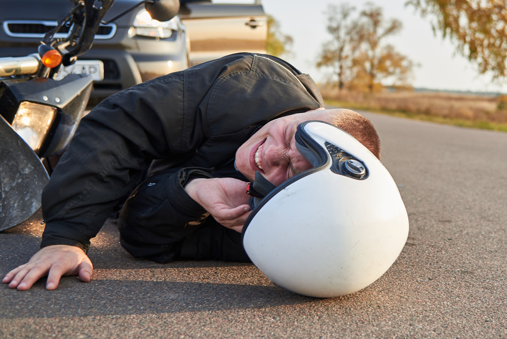 Injured motorcyclist lying on the road beside a motorcycle after a traffic accident, wearing a helmet and protective riding gear.